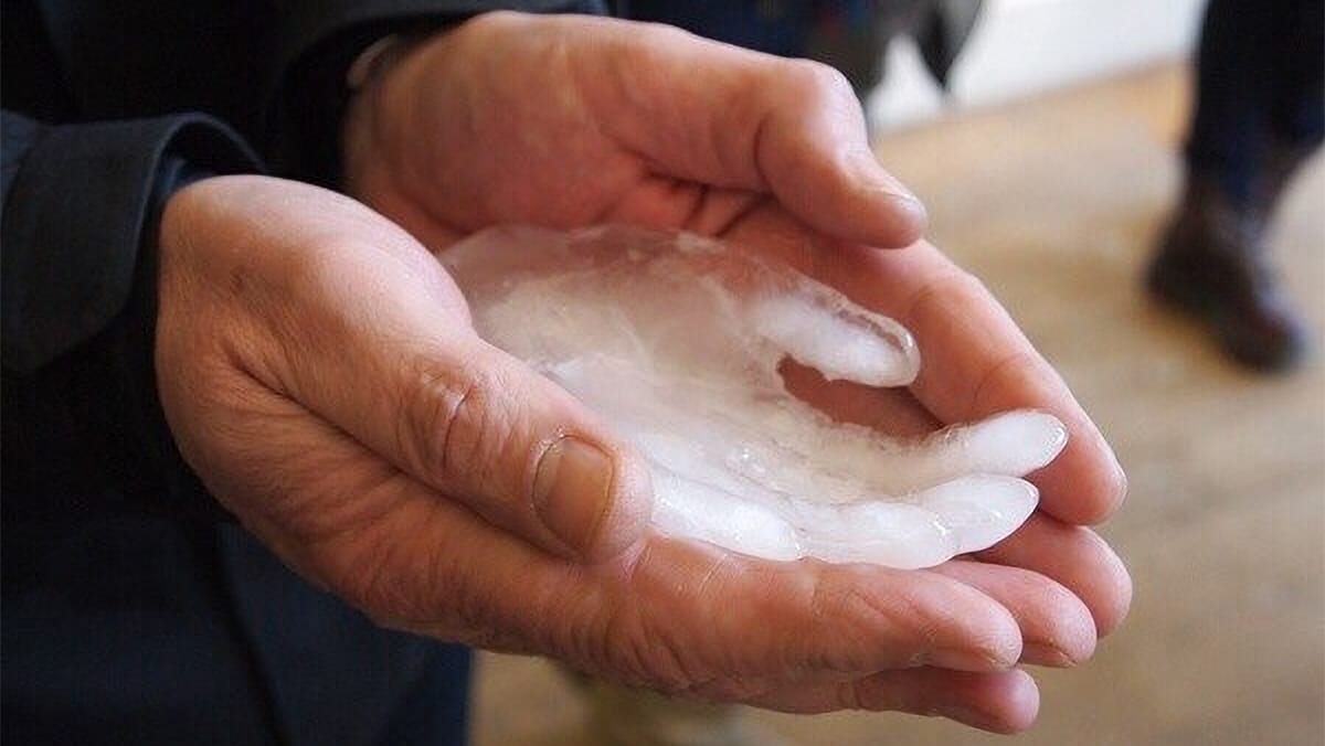 A close-up of a person cupping their hands under a small ice sculpture of a hand.